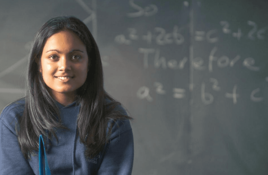 A girl sits in front of a blackboard with several equations on