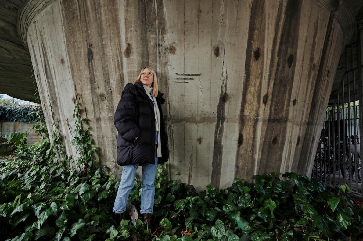Artist Katie Paterson stood next to her artwork on a concrete structure.