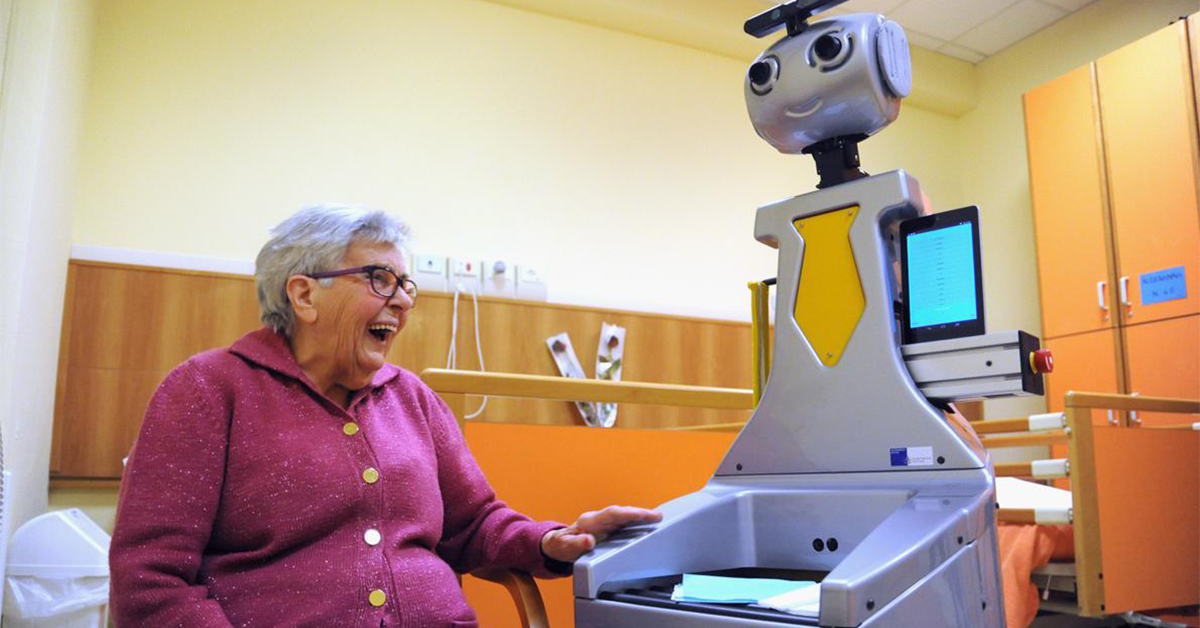 An elderly woman sat down laughing beside a robot.