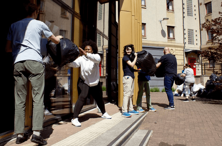 Volunteers in a line passing rubbish bags out the door to a large pile