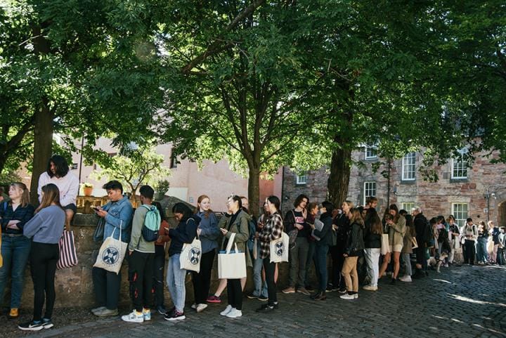 students queuing for the free shop. Standing under trees.