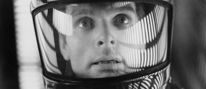 Astronaut gazes out of helmet, lights reflected on glass