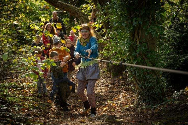 Educator leads children and families on a woodland adventure holding onto a rope.