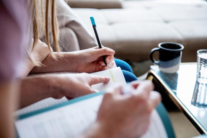 A close up of two sets of hands over notebooks. One set is helping the other learn something.