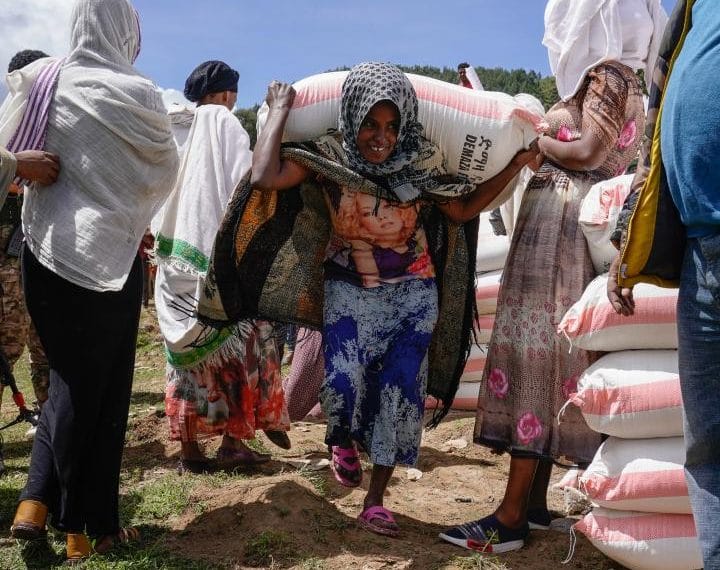 A woman carries a bag of wheat flour that was part of her food aid package
