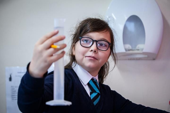 A school child measures water in a cylinder