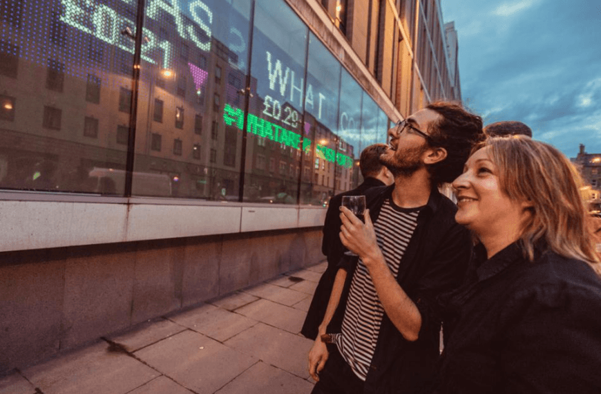 People looking at an LED board showing the cost of each word in George Orwell's 1984