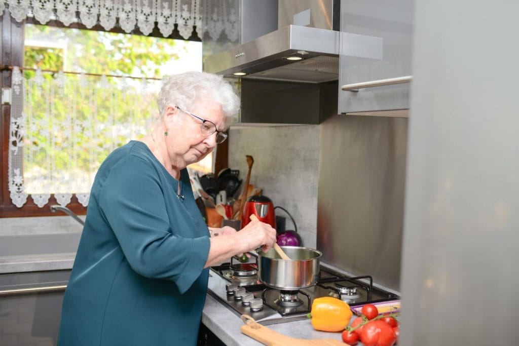 Older woman cooking in the kitchen. She is stirring a pot.