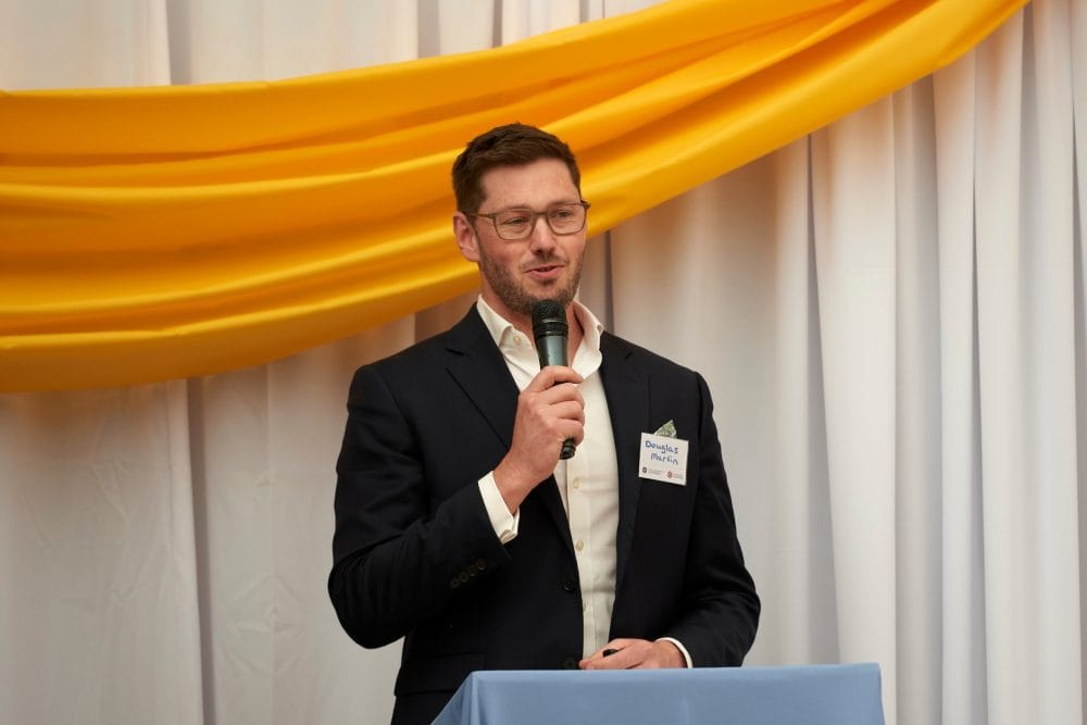 Photograph of Douglas Martin holding a microphone while standing at a podium as he introduces the students who won awards at the most recent student enterprise awards ceremony.