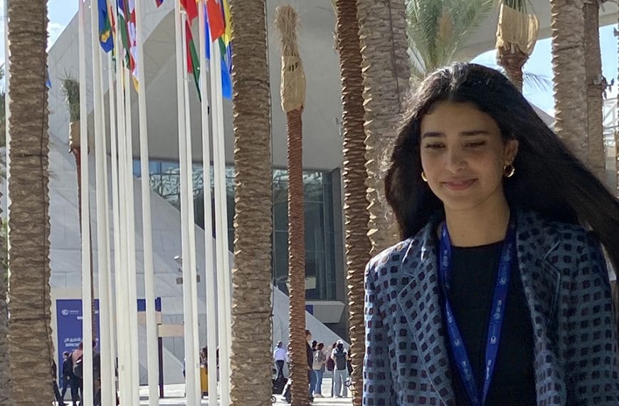 A young woman walking outside COP28 past a row of trees and international flags