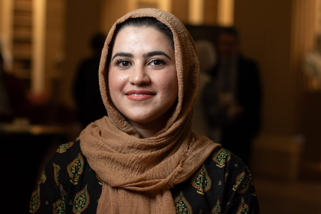 A portrait of Kainat Riaz, a woman wearing a headscarf and smiling at the camera.
