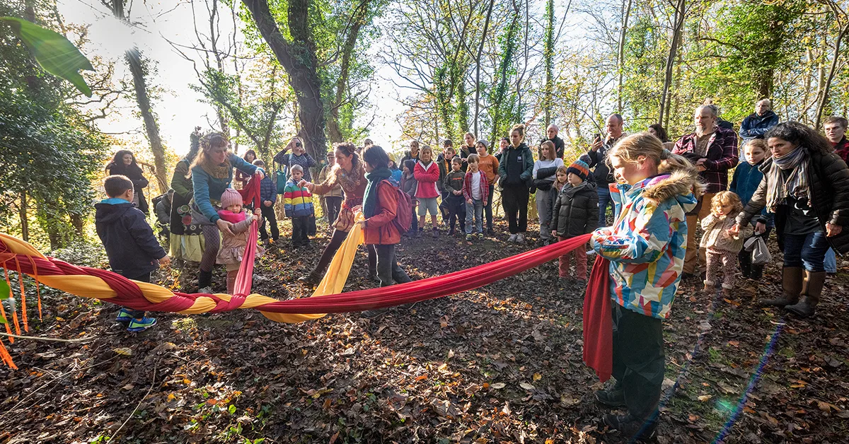 Children braiding a long length of yellow and red fabric in the woods.