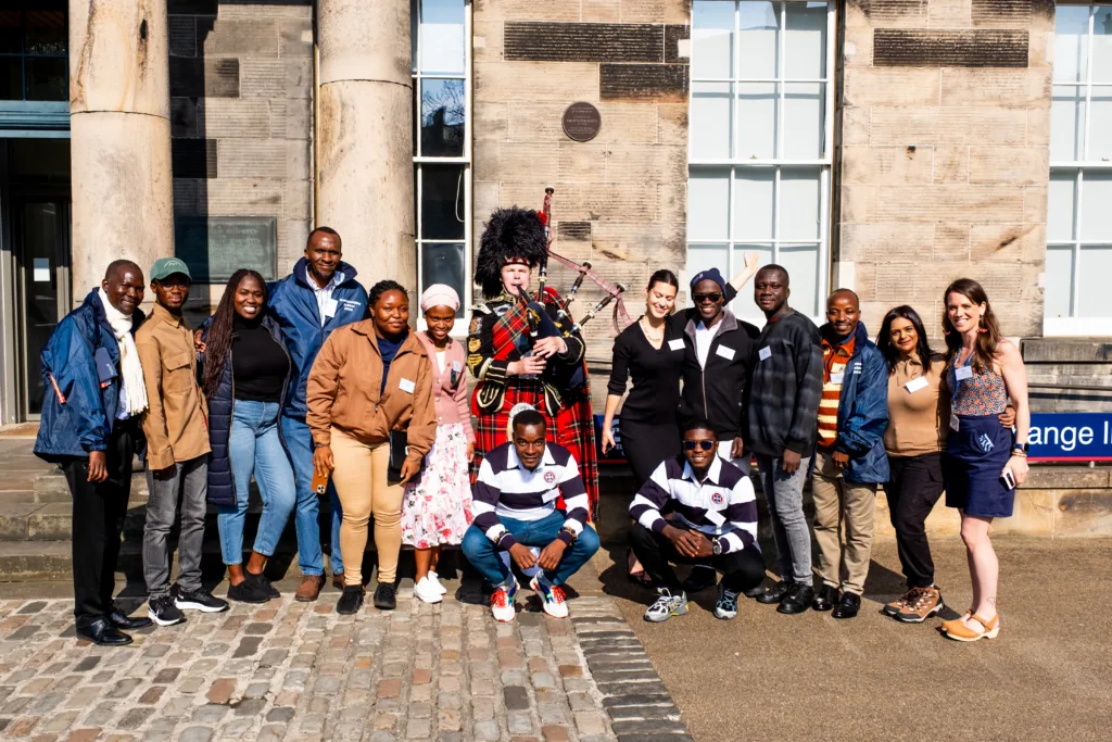 A group of WESAF Fellows gather together for a photo with a Scottish piper outside University buildings in Edinburgh.