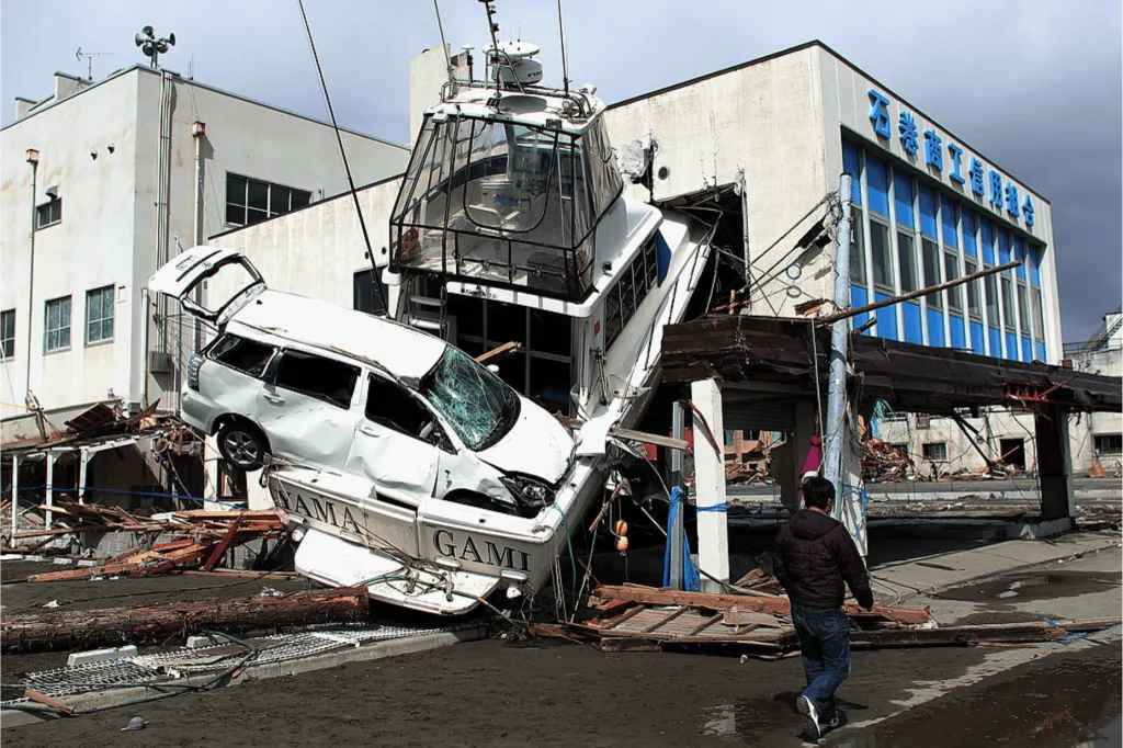 A man walks past a car wedged into a boat on March 18, 2011 in Ishinomaki, Japan.