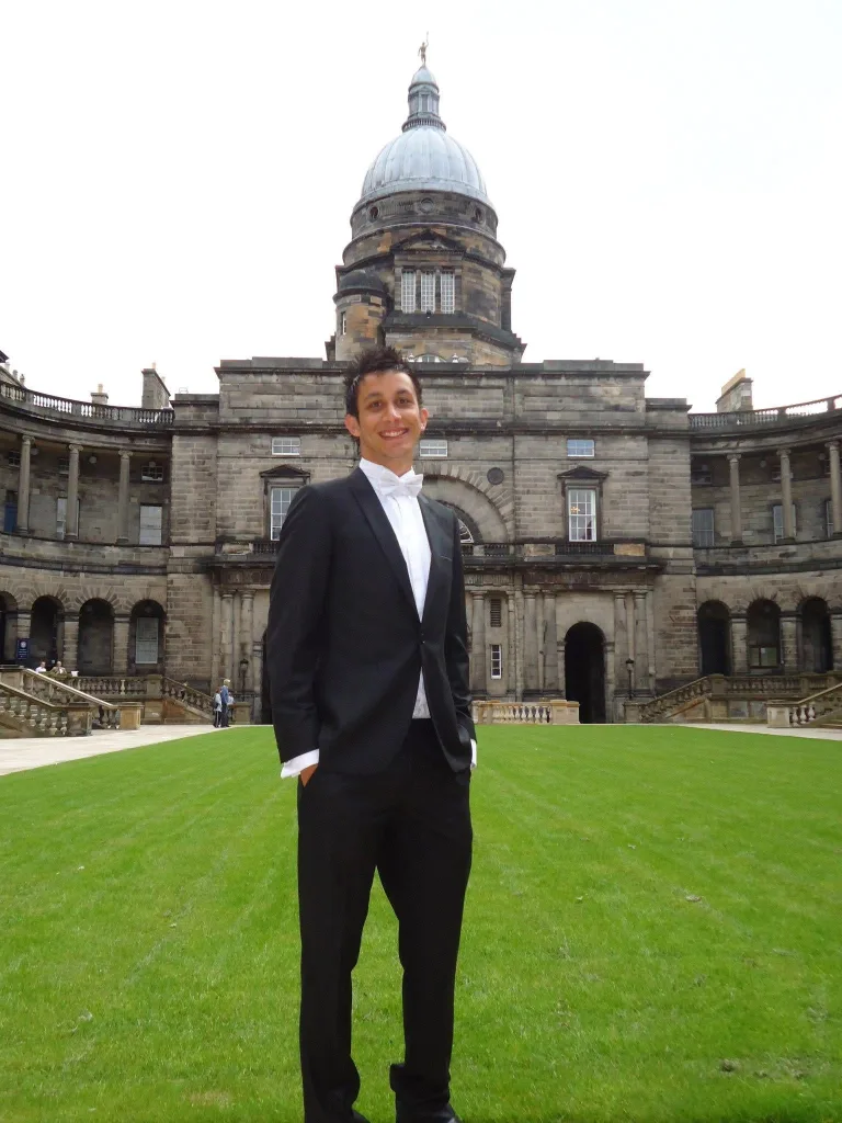 A male University of Edinburgh graduate standing in front of the Old College Quad