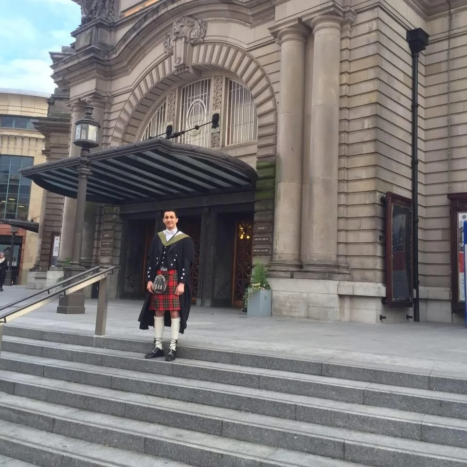 A male University of Edinburgh graduate posing in a kilt and graduation robes.