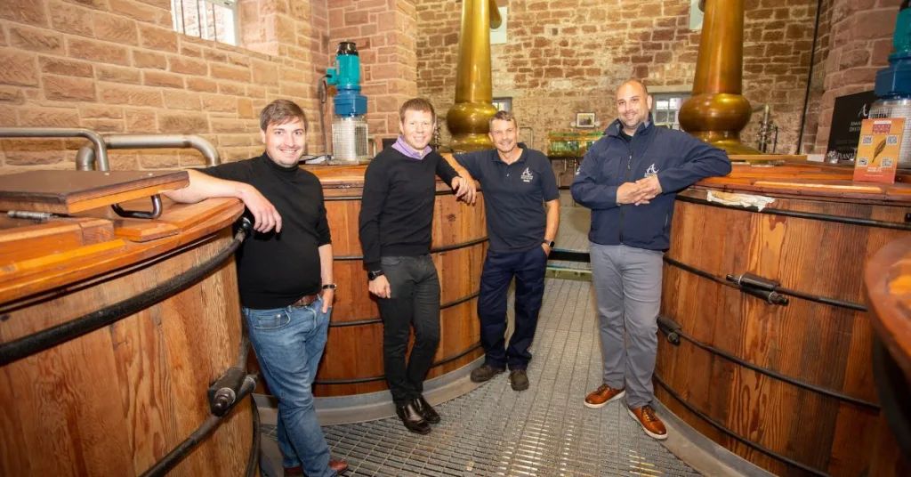 Four men standing beside whisky barrels at Annandale Distillery in Dumfries and Galloway