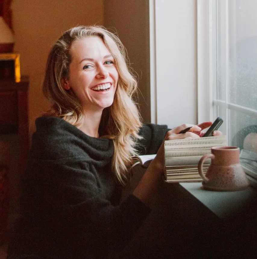 A woman pictured holding a phone and smiling at the camera 