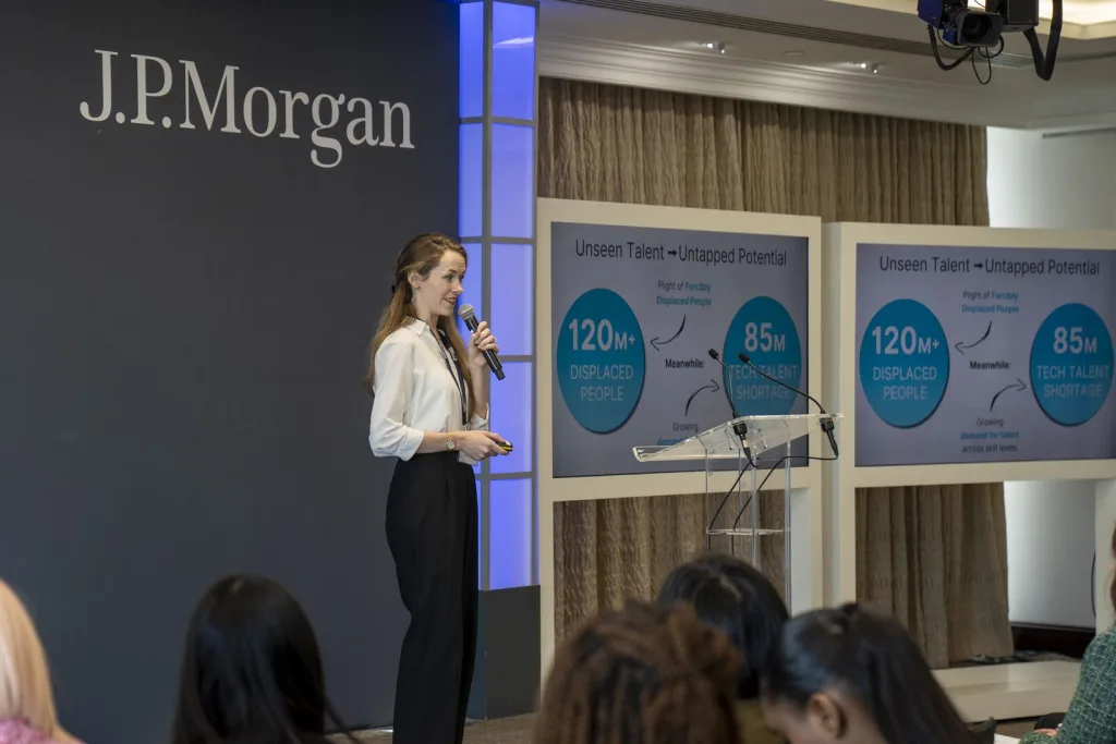 A woman standing holding a microphone on stage at the JP Morgan Founders Perfect Pitch programme