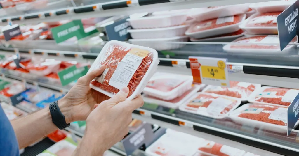 A person holding a packet of mince in the meat aisle of a supermarket 