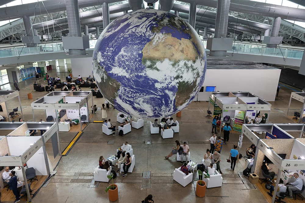Looking down at delegates sitting and moving around stalls inside the COP30 venue with a giant globe suspending from the ceiling.