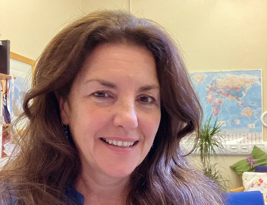 Professor Liz Grant smiling towards the camera with a world map on the wall in the background.