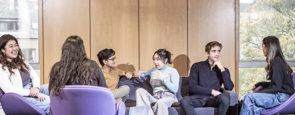 A photograph shows six animated students in a group setting, all engaged in discussion. They are seated in an open-plan area, inside the School of Literature, Languages and Cultures.