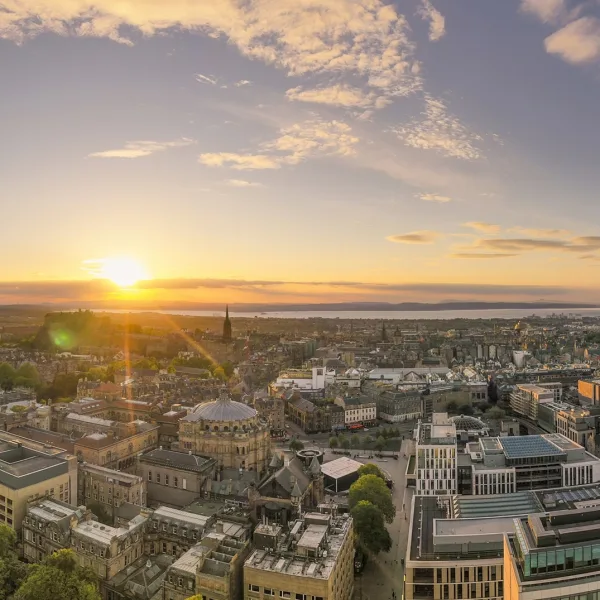Panoramic image of Edinburgh, with the sun shining just above the urban skyline.