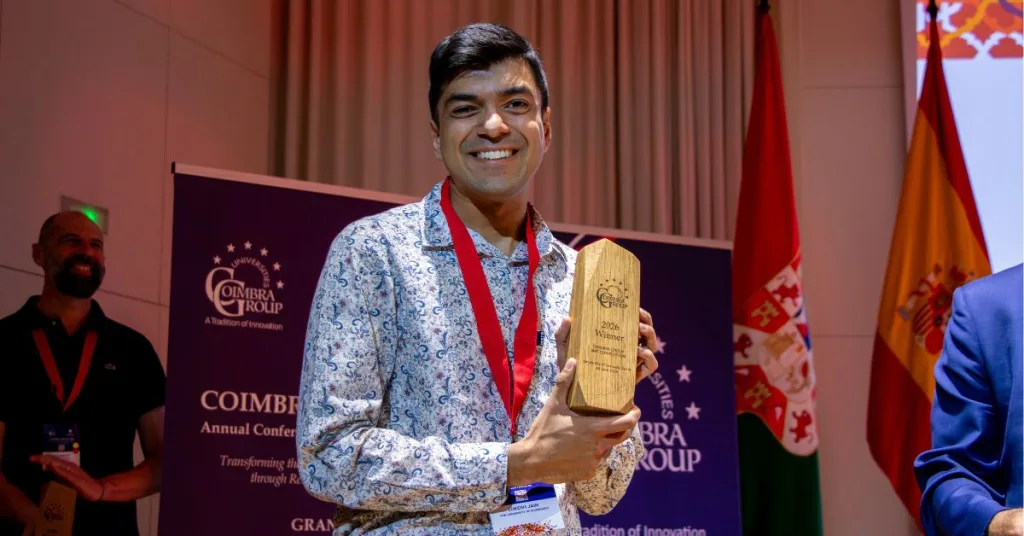 A man smiling at the camera with a plaque from the Three-Minute Theis competition