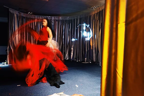 A performance artist in red flowing dress moving with draped silver stage curtains hanging in a semi circle the background.