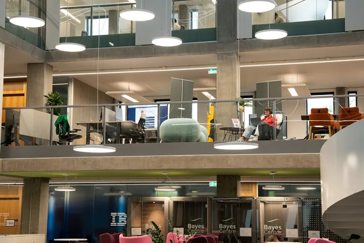 Internal image of the Bayes Centre showing 3 floors with desk spaces and someone working at a laptop