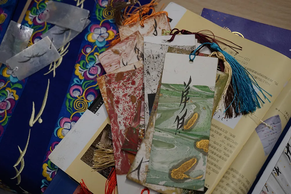 A close up of Jiaya Chen's workshop art materials including colourful card, tassels, textiles and an open book showing script.