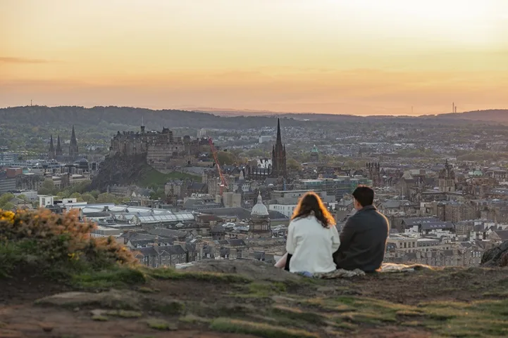 Two people sitting on Salisbury Crags looking over the city of Edinburgh with Edinburgh Castle in the centre
