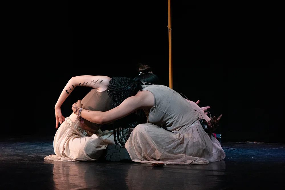 Jiayi Chen and Junnan Cheng sit on stage facing one another with their arms curved towards each other during a performance of Nüshu at the Edinburgh Fringe