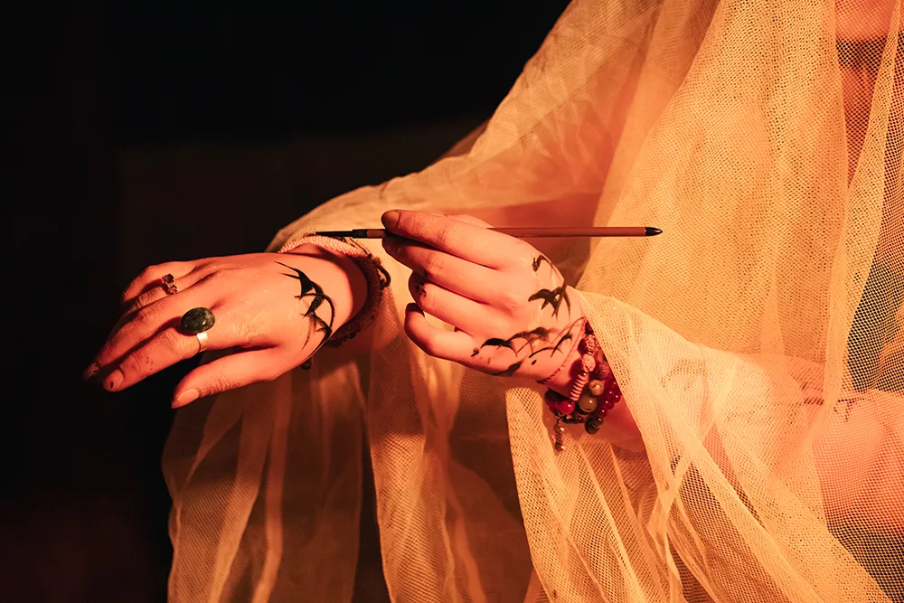 Close up of a hand using a calligraphy brush to paint script onto the other hand shown
