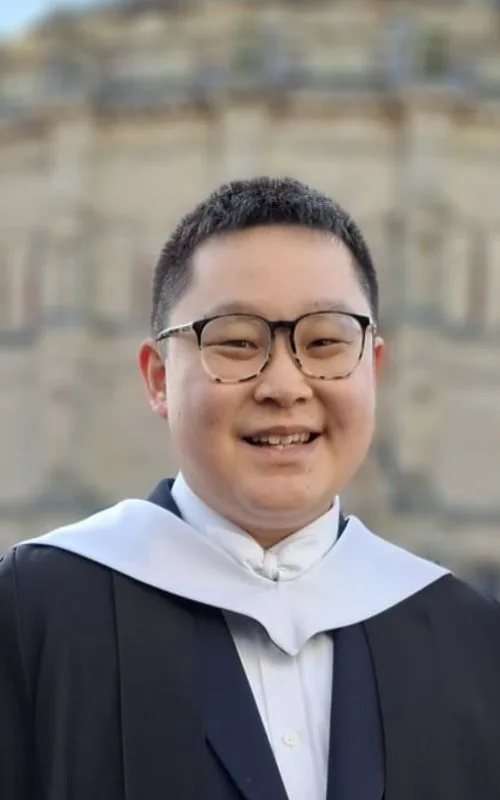 A student in graduation robes smiling at the camera