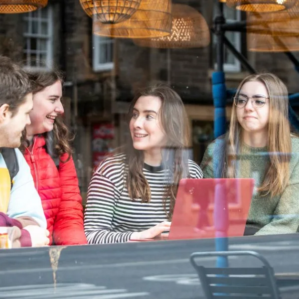 Students photographed through a window. They are sitting down and looking at a laptop.