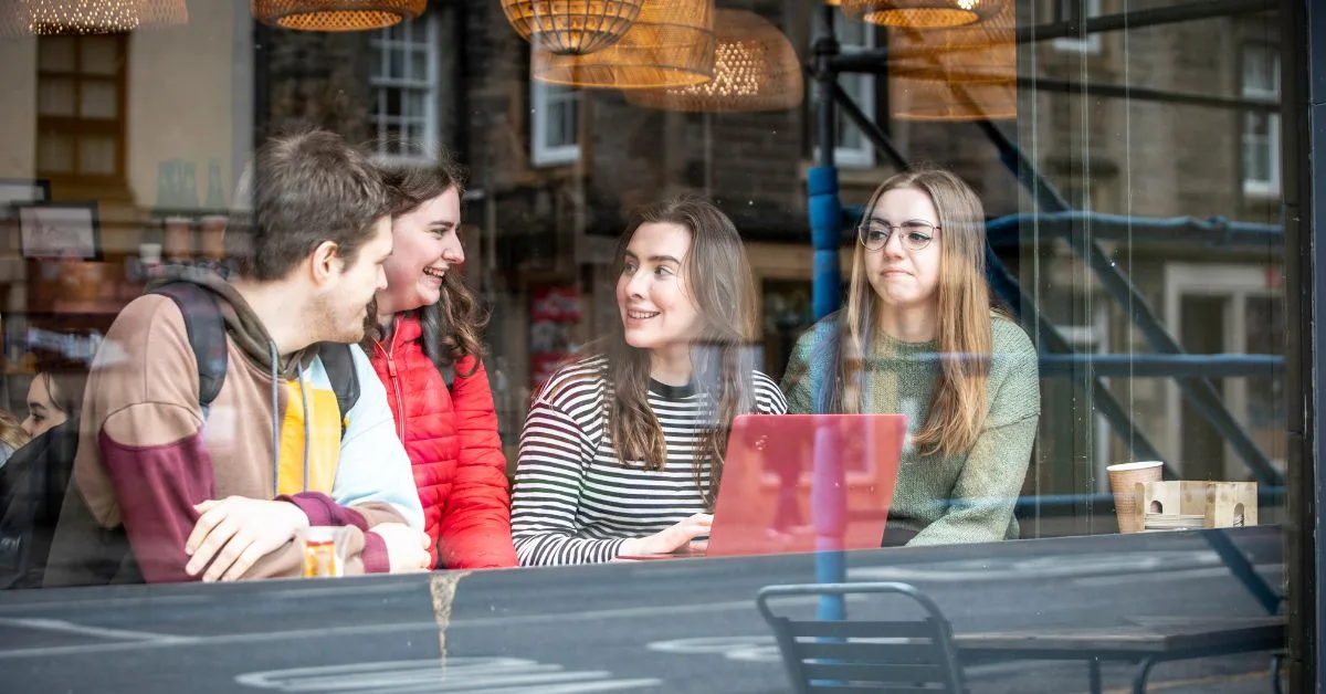 Students photographed through a window. They are sitting down and looking at a laptop.