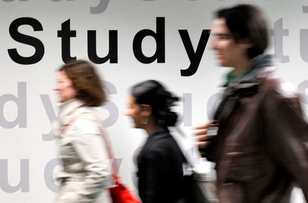 Students walking in a university building. Text says "Study" on the wall.